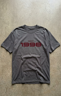 Gray t-shirt with 'Since 1998' text on a concrete surface