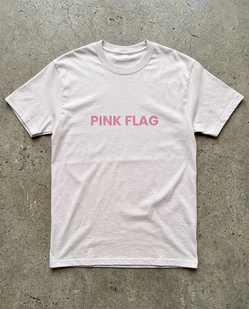 White t-shirt with 'PINK FLAG' text on a concrete surface