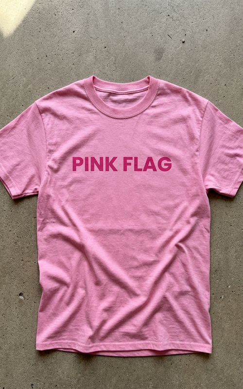 Pink t-shirt with 'PINK FLAG' text on a gray surface